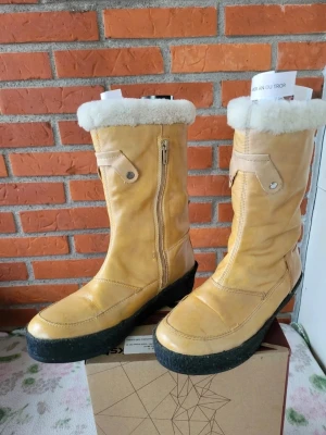 Beige skinnstövlar från Vagabond 37 - Säljer ett par beige stövlar från Vagabond med mjuk päls runt skaftet och grov svart sula. Stövlarna har dragkedja på sidan och är tillverkade i skinn med detaljer i syntet. Perfekta för kalla dagar med sin fluffiga insida och höga skaft.