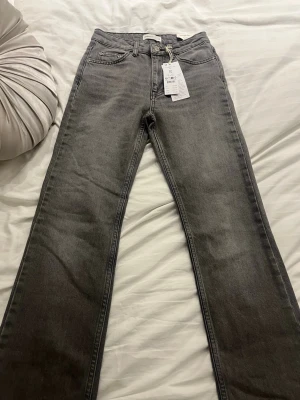 Grå full length flare jeans, storlek 32 - Snygga grå jeans från Perfect Jeans i modellen full length flare. De har klassisk femficksdesign, hög midja och raka ben med utsvängd avslutning. Materialet är mjukt jeans-tyg som sitter bekvämt och ger en cool vibe. Perfekt för dig som gillar retro och trendiga silhuetter. Och de är även helt nya och oanvända 