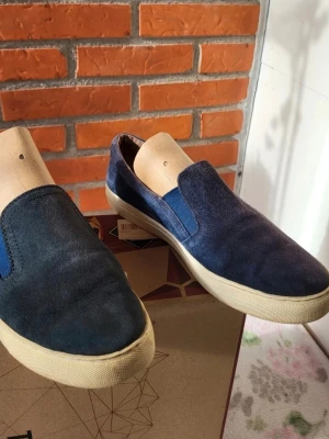 Blå mocka loafers från Dasia - Säljer ett par snygga loafers från Dasia i marinblå mocka med elastiska partier på sidorna för enkel påtagning. Skorna har en platt, ljus sula och rund tå. Insidan är i skinn med komfortdesign. Perfekt för dig som gillar stilrena och bekväma skor. Fin olika nivåer av navy på skorna