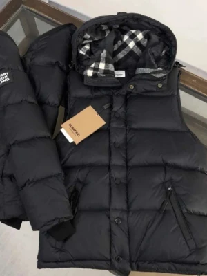 Burberry puffer jacka  - Svart pufferjacka från Burberry med rutigt foder i huvan. Jackan har både dragkedja och knappar framtill, samt två sidofickor med dragkedja. Klassisk Burberry-logga på ärmen och quiltad design. Perfekt för kalla dagar och riktigt snygg stil.