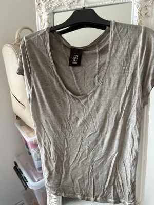 Grå t-shirt från Thom/Krom - Säljer en grå t-shirt från Thom/Krom med avslappnad passform och djup rund halsringning. T-shirten är kortärmad och tillverkad i mjuk bomull, perfekt för en chill och enkel stil. Snygga råa sömmar ger en cool edge till looken.