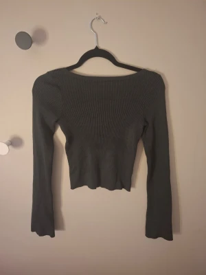 Mörkgrå ribbad topp från H&M - Säljer en mörkgrå ribbad topp från H&M i storlek 158/164. Toppen har långärmad design, croppad passform med öppen rygg. 💕