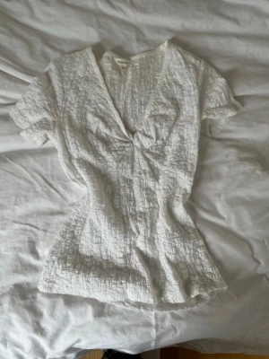 Vit blus med knut från Dobber - Säljer en vit blus från Dobber i storlek XS. Toppen har korta ärmar, v-ringning och en snygg knut framtill. Inga defekter, men är dock lite, lite gul runt halsen vilket man kan se på sista bilden. Men ärligt ser man det knappt❤️