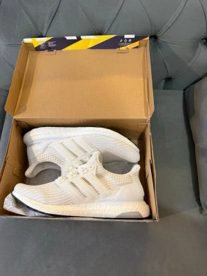 Vita Adidas Ultra Boost  - Säljer ett par fräscha Adidas Ultra Boost i helvitt. Skorna har stickad ovandel i mesh, klassiska tre ränder på sidan och Boost-sula för maxad komfort. Perfekta för dig som vill ha stilrena och bekväma sneakers till vardagen. Kan Levereras i kartong.