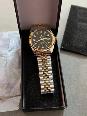 Ingen väst på bilderna - En fin guld och silver klocka som är rostfri och vattentät klockan är tung så den ser ut riktigt bra, och om du köper den och den var inte tung så kan du bara returnera direkt. Helt ny plast finns fortfarande runt kedjan.