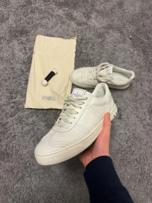 Valentino Garavani vita sneakers i skinn - Säljer ett par vita Valentino Garavani flycrew sneakers i skinn med nitar runt hälen och kamouflagemönstrad sula. Klassisk rund tå, snörning och stilren design. Kommer med dustbag och extra skosnören. Alla nitar sitter på plats och skicket är 9/10 pris kan diskuteras