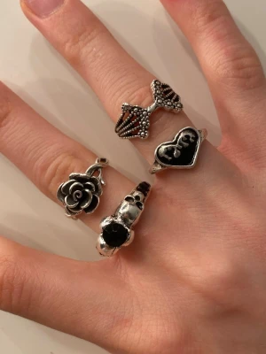 Snygga silverfärgade ringar - Coola ringar i silverfärgat material med unika detaljer som ger en edgy vibe. En har en ros, en ett svart hjärta, en med döskallar och en med ett coolt mönster. Ej äkta silver! styckpris 12kr, alla för 30kr 🫶