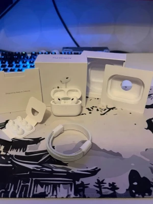 AirPods Pro 2 - Apple AirPods Pro med laddningsetui, extra öronkuddar och originalförpackning. Produkten ser ut att vara i mycket gott skick utan synligt slitage. Perfekt för trådlös musik och samtal med aktiv brusreducering och hög ljudkvalitet.