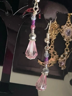  Hangjorda, långa örhängen med rosa droppar - Säljer ett par snygga handgjorda örhängen med silver s 925 krokar och hängande pärlor i  rosa och lila toner. De har en droppformad rosa pärla längst ner och små glittriga detaljer längs hela hänget. Perfekta för dig som gillar färg och vill sticka ut lite extra. De stora dropparna är facettslipatglas de små (runda) halvädelstenar.