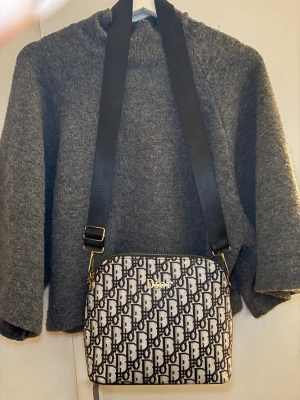 Svartvit axelväska från **** - Säljer en snygg axelväska med bred svart rem och guldiga detaljer. Väskan har ett tydligt mönster i svart och vitt över hela ytan och stängs med dragkedja upptill. Perfekt storlek för det viktigaste och ger en lyxig vibe till din outfit.