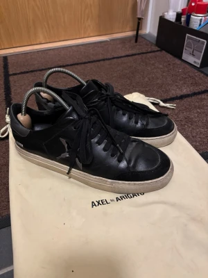 Svarta sneakers från Axel Arigato - STEAL! Snygga svarta sneakers från Axel Arigato med broderad fågel på sidan och kontrasterande beige sula. Skorna är handgjorda i Portugal och är tillverkade i läder med detaljer i mocka. En dustbag tillkommer med skorna. Nypris: 2750kr. Mitt pris: 499kr. Använda med i välbehållet skick. Har några få slitningar. Har du frågor eller funderingar, tveka inte på att höra av dig!