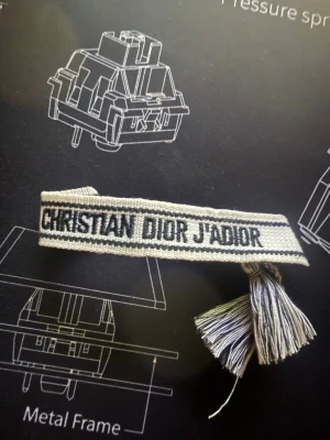 Dior armband, vit. - Stilig Christian dior armband men svart text och vit bas. Går att ändra storlek med snören på baksidan, perfekt skick inget fel på styngen.