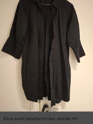 Svart lång skjorta från Ellos, strl 40 - Säljer en svart lång skjorta från Ellos i storlek 40. Skjortan har knappar framtill, trekvartsärmar med bred manschett och en lös, avslappnad passform. Perfekt till lager på lager och enkel att styla med olika accessoarer.