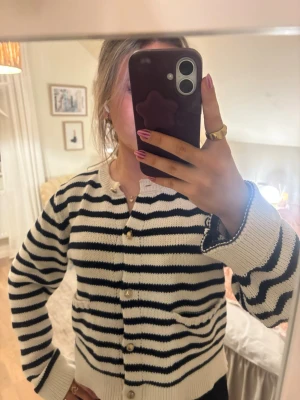 Randig stickad kofta med knappar - Säljer en stickad kofta med svarta och vita ränder. Koftan har guldiga knappar framtill, två små fickor och ribbade muddar. Perfekt för lager-på-lager och har en klassisk, chill vibe.