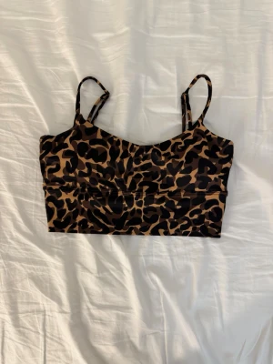 Leopardmönstrad träningstopp från am’n XS - Säljer en snygg leopardmönstrad  träningstopp från am’n i storlek XS. Toppen har smala justerbara axelband och är croppad i modellen. Materialet är mjukt och stretchigt med 73% polyester och 27% spandex. Perfekt för dig som gillar djurmönster och vill sticka ut.