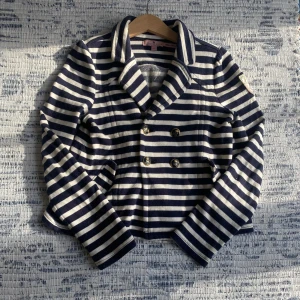 Randig kavaj/kofta från Juicy Couture - Säljer en randig kofta från Juicy Couture i marinblått och vitt. Kavajen har en dubbelknäppt design med svarta och guldiga knappar och en rosett på ryggen. Tvättas innan frakt. Pris kan diskuteras.