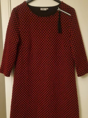 Röd och svart mönstrad klänning  - Säljer en cool kortklänning från Isolde i storlek L. Klänningen har ett rött och svart geometriskt mönster, trekvartsärm och en snygg silverfärgad dragkedja med svart band vid axeln. Materialet känns mjukt och har lite struktur, perfekt för dig som gillar att sticka ut. Kolla gärna in mina andra annonser! 