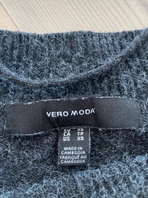 Mörkgrå stickad tröja Vero Moda - Mysig mörkgrå stickad tröja från Vero Moda i storlek XS. Tröjan har lång ärm, rund hals och ribbade muddar vid ärmslut och nederkant. Materialet är stickat och ger en fluffig känsla, perfekt för kyliga dagar.