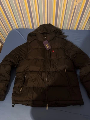 Polo Ralph Lauren jacka  - Säljer en svart pufferjacka från Polo Ralph Lauren med huva och dragkedjor. Den är helt ny oanvänd det är storlek M på den 