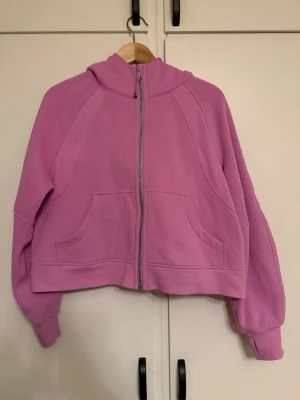 Lulelemon  - Överdimensionerad passform, midjelängd En överdriven passform som känns extra rymlig Inte för kort, inte för lång, precis runt midjebandet Produktegenskaper Framfickor med invändig kortficka Dragkedja håller skavet borta Elastisk dragkedja som även fungerar som hårband i nödfall och tumhål. Stl M/L (EU 38-44)