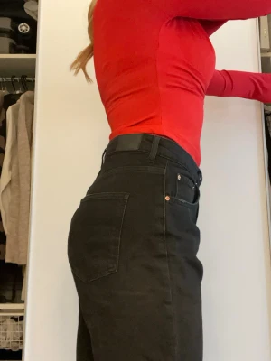 Svarta bootcut jeans med slits - Säljer ett par svarta jeans med bootcut-snitt och hög midja. Jeansen har klassiska fem fickor, knapp och dragkedja framtill samt slits vid bensluten för extra edge. Materialet är jeans och passformen är loose. Perfekta för dig som gillar en chill och trendig stil. Lite stora på mig så bilden kan vara lite missvisande 