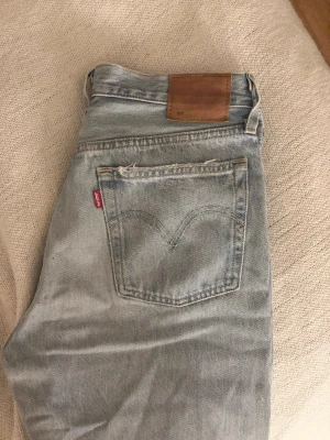 Levi's ljusblå raka jeans - Levis 501 - Ljusblå jeans från Levi's med klassisk femficksdesign och raka ben. Jeansen har den ikoniska röda Levi's-taggen på bakfickan och läderpatch i midjan. Tillverkade i bomull med vintagekänsla och snyggt slitna detaljer. Säljer då de tyvärr är för stora. Storlek W30 L32, passar de som har M/L