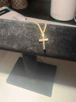 Guldigt halsband med korshänge - Snyggt halsband i guldfärg med ett enkelt kors som hänge. Kedjan är tunn och stilren, perfekt för dig som gillar minimalistiska smycken. Passar till många olika looks och är lätt att matcha med andra accessoarer.