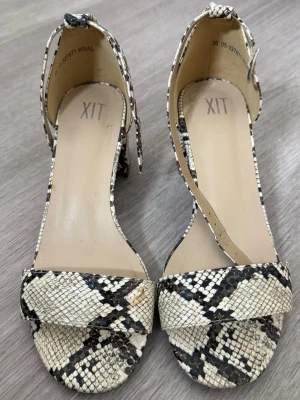 Mönstrade pumps från XIT - Snygga pumps från XIT med ormmönster! Bred rem över tårna och ett justerbart spänne runt ankeln. Använda en gång! Säljer eftersom jag aldrig använder klackskor. Storlek 36, passar även mig som har storlek 36,5.