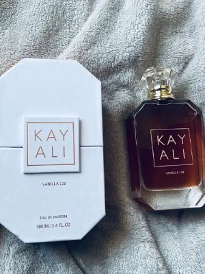 Kayali Vanilla | 28 Eau de Parfum - Kayali Vanilla | 28 Eau de Parfum med en elegant parfym flaska. Doften har en varm, djup vanilj doft och kommer i en vit, stilren flaska med förpackning. Flaskan rymmer 100 ml 