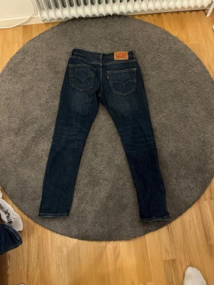Mörkblå Levi's jeans med raka ben - Säljer ett par klassiska mörkblå jeans från Levi's med raka ben och femficksmodell. Jeansen har tydliga sömmar, läderpatch bak i midjan och den ikoniska röda Levi's-lappen på bakfickan. Perfekta till en avslappnad streetwear-look.
