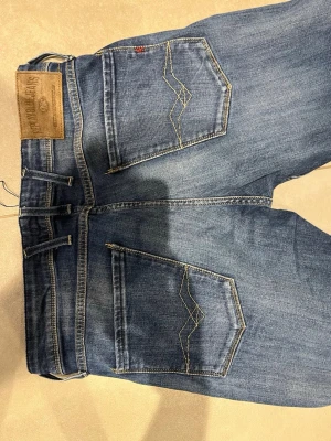 Blå jeans från Nudie Jeans - Säljer ett par klassiska blå jeans från replay med snygga kontrastsömmar och femficksmodell. Jeansen har en rak passform och coola detaljer på bakfickorna. Tillverkade i slitstark denim med en tvättad look.