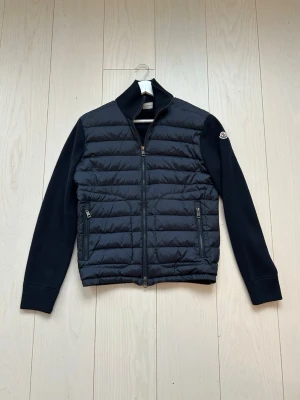 Moncler cardigan - Säljer en navy blå quiltad jacka från Moncler med ribbad hög krage och muddar. Endast testad, inga skador eller tecken på användning!