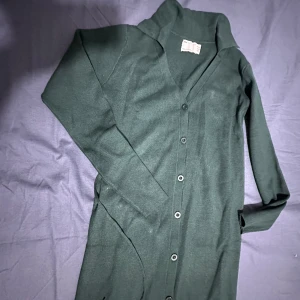 Stickade midiklänning  - Stickade miniklänning med öppen krag och knyt i midjan. Ny utan prislappen 