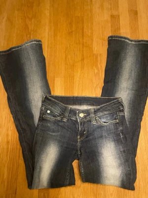 Mörkblå bootcut jeans Cheap Monday - Snygga mörkblå bootcut jeans från Cheap Monday med slitningar och ljusare partier framtill. Klassisk femficksmodell och tydliga kontrastsömmar. Perfekta för en avslappnad och trendig look.