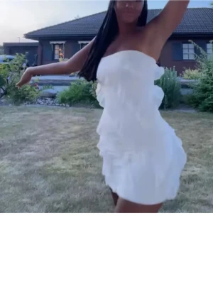 Vit volangklänning axelbandslös studentklänning  - Supersöt vit kort klänning med volangdetaljer och axelbandslös design. Perfekt för sommarens alla tillfällen exempelvis studenten!. Lätt och luftig känsla med snygg passform. Första bilden är lånad, stl M säljer då jag hittat en annan inga defekter 💕