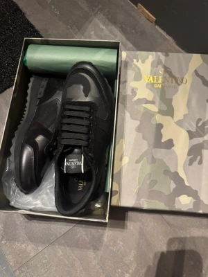 Valentino rockrunners - Snygga svarta sneakers från Valentino Garavani med coolt kamouflagemönster och detaljer i läder och textil. Skorna har svarta snören och en robust sula med mönster för extra grepp. Perfekta för dig som vill sticka ut med stilrena och exklusiva sneakers.