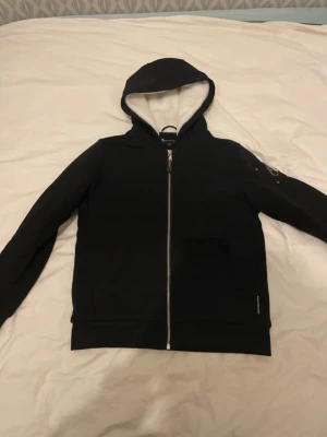 Moose knuckles Bunny jacket  - Svart vindjacka från moose knuckles  med hel dragkedja, huva och två fickor framtill. Jackan har quiltat foder och vit insida på huvan. Perfekt för blåsiga dagar och har en stilren look.