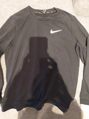 Svart sweatshirt från Nike - Mycket gott skick. En stilren svart sweatshirt från Nike med klassisk vit Swoosh-logga på bröstet. Tröjan har rund halsringning och långa ärmar. Perfekt för en sportig och avslappnad look. Tillverkad i mjukt material för extra komfort.