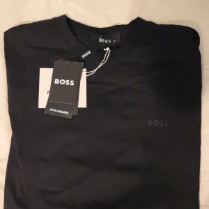Svart t-shirt från BOSS Athleisure - Snygg svart t-shirt från BOSS Athleisure med diskret logga på bröstet. Klassisk rund halsringning och stilren design som passar till allt. Tillverkad i mjuk bomull för skön känsla hela dagen.