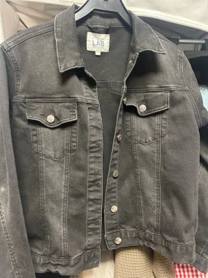 Svart jeansjacka - Snygg svart jeansjacka från LAB Industries med klassisk krage, två bröstfickor med knappar framtill. Jackan har en rak passform och tydliga sömmar som ger en cool vintagekänsla. Perfekt att slänga över en hoodie eller t-shirt. Storlek 164 passar mig som har XS/S.