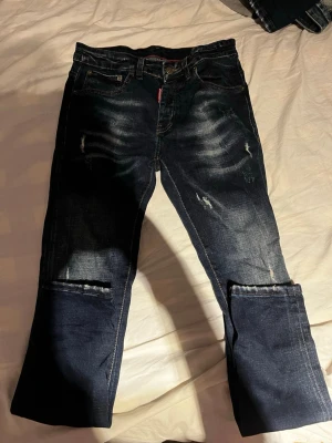 Dsquared2 jeans - Mörkblå slim jeans från Dsquared2 med coola slitningar och detaljerade revor på benen. Jeansen har klassisk femficksdesign, röd logotagg vid fickan och är tillverkade i Italien. Perfekta för dig som gillar en edgy streetstil.
