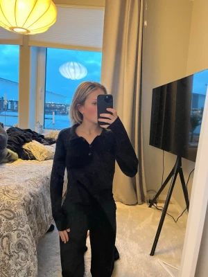 Svart ribbad långärmad tröja - Svart långärmad tröja med ribbad struktur och knappar vid halsringningen. Tröjan har en figurnära passform sitter som en xs/s