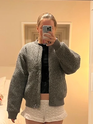 Grå hm bomberjacka - Mysig grå bomberjacka i teddy-material med ribbade muddar och krage. Jackan har dragkedja framtill och en extra ficka med dragkedja på ena ärmen. Storleken är xxs men skulle säga att det mer är en xs eller s i storleken💗