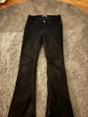 Svarta bootcut jeans från Gina tricot - Säljer ett par svarta bootcut jeans med klassisk femficksmodell och svarta sömmar. Jeansen har utsvängda ben och normal midja. Perfekta för dig som gillar en tidlös och snygg look.