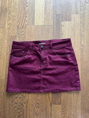 Vinröd kortkjol från Terranova - Vinröd kortkjol från Terranova i klassisk jeansmodell med fem fickor och bälteshällor. Kjolen har knapp och dragkedja framtill och är tillverkad i bomullsmaterial. Perfekt för dig som gillar en enkel men snygg stil. Skriv för fler bilder!