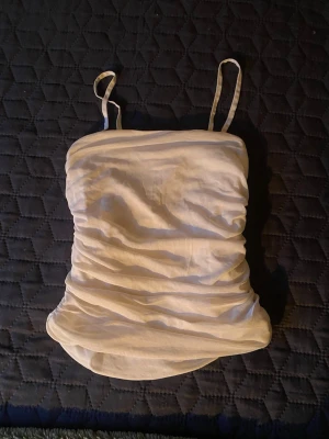 Vit rynkad linnetopp med smala band❕ - Snygg vit linnetopp med smala axelband och rynkade detaljer längs sidorna. Toppen har en omlottliknande form och är perfekt för en fräsch och stilren look. Passar till många olika outfits och är lätt att matcha🎐