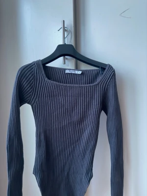 Grå ribbstickad tröja från NA-KD - Säljer en grå ribbstickad tröja från NA-KD med lång ärm och fyrkantig halsringning. Tröjan är figurnära och har en modern, stilren look som passar perfekt till jeans eller kjol.