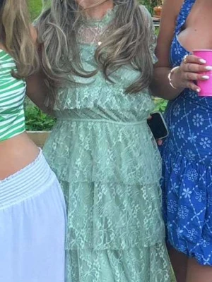 Ljusgrön spetsklänning med volanger - Romantisk ljusgrön långklänning i spets med volangdetaljer och transparent överdel. Klänningen har korta ärmar och rund halsringning. Perfekt för sommarens alla tillfällen.