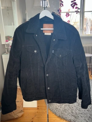 Svart  Manchester teddyjacka från Levi's - Svart manchester jacka från Levi's med mjukt teddy foder inuti. Klassisk jeansjackemodell med knappar framtill och två bröstfickor med lock.
