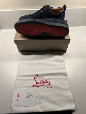 Marinblå Christian Louboutin - Stilrena sneakers från Christian Louboutin med klassisk röd sula och snörning. Ovandelen är i mocka och skon har en rund tå. Perfekta för dig som vill ha en lyxig och ikonisk sneaker med unik design.